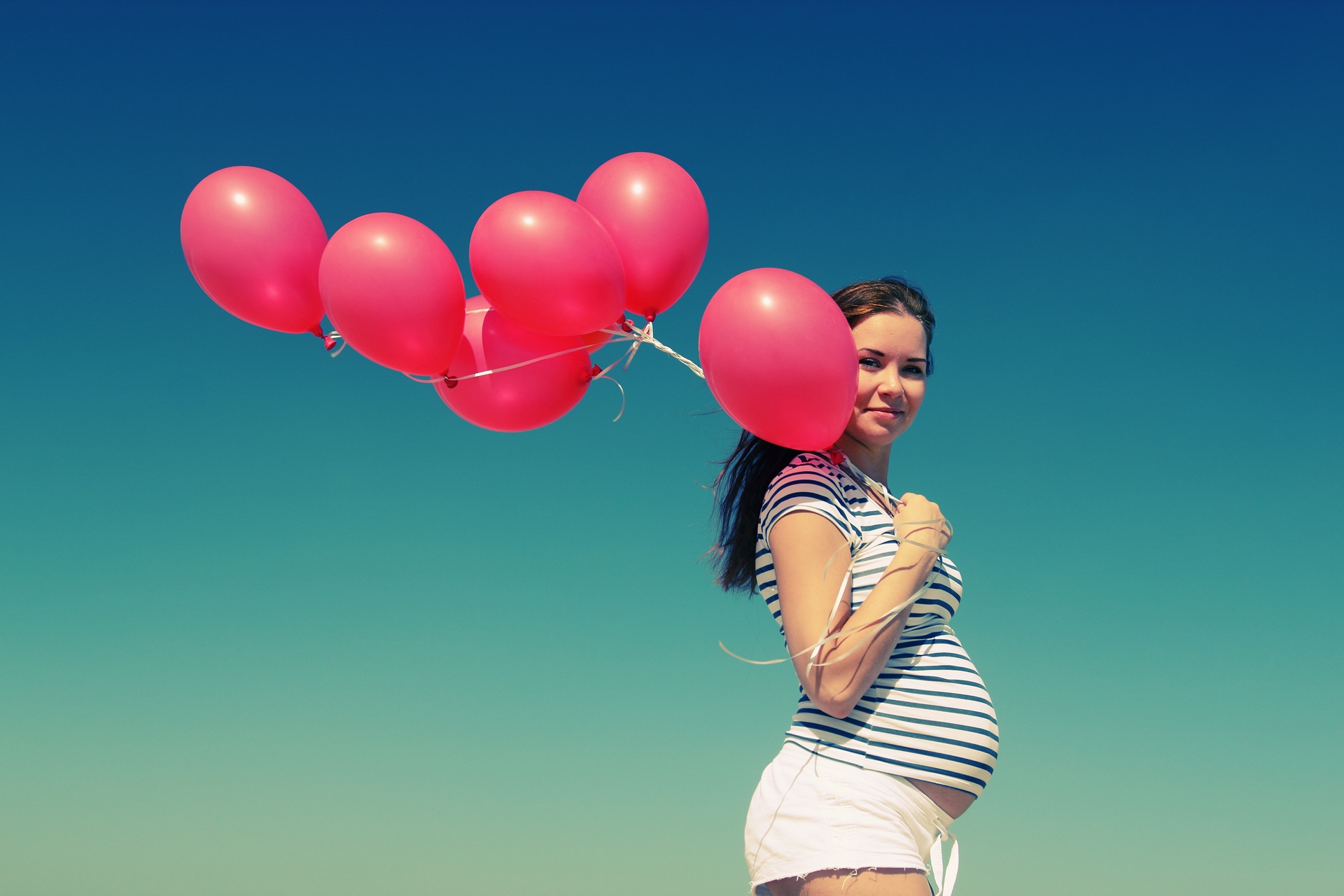 young pregnant woman holding red balloons