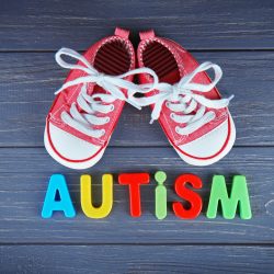 Word AUTISM with kids shoes on wooden background